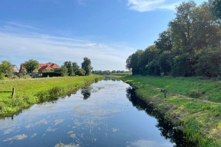 Natuurlijk landschap met een riviertje en een boerderij aan de horizon.