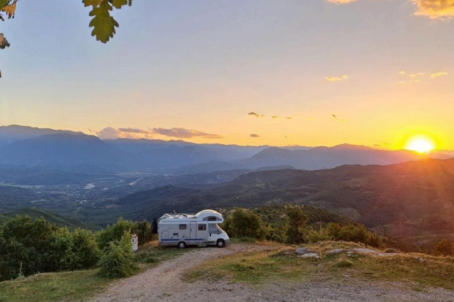 Vergezicht met een camper in een bergachtig landschap met een ondergaande zon.